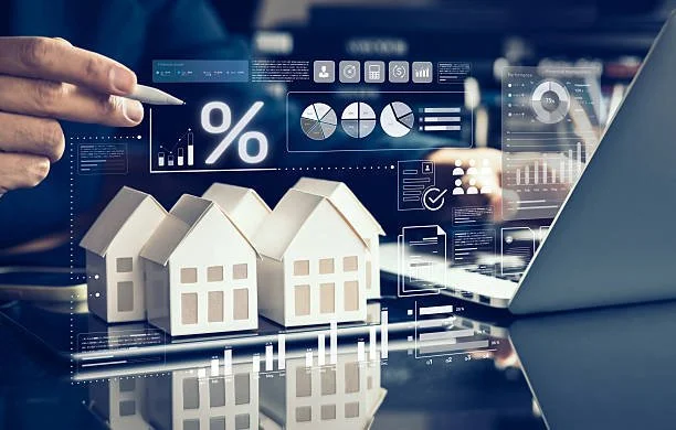 Digital financial analysis with model houses, charts, and graphs on a computer screen, with a person's hand pointing at the screen.