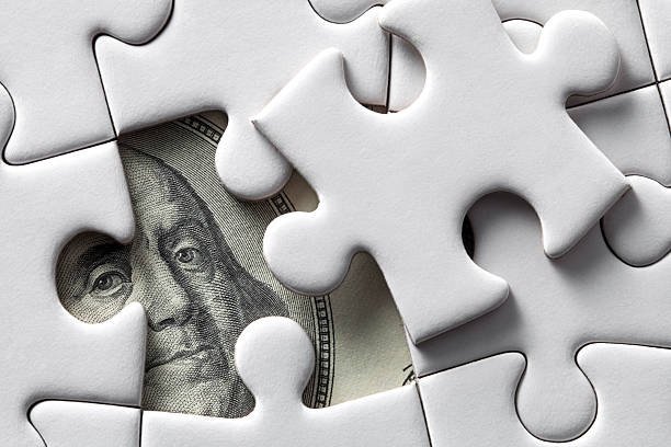 A close-up of a partially assembled puzzle with a piece depicting Benjamin Franklin's face from a hundred-dollar bill, representing a dollar sign, surrounded by white puzzle pieces.