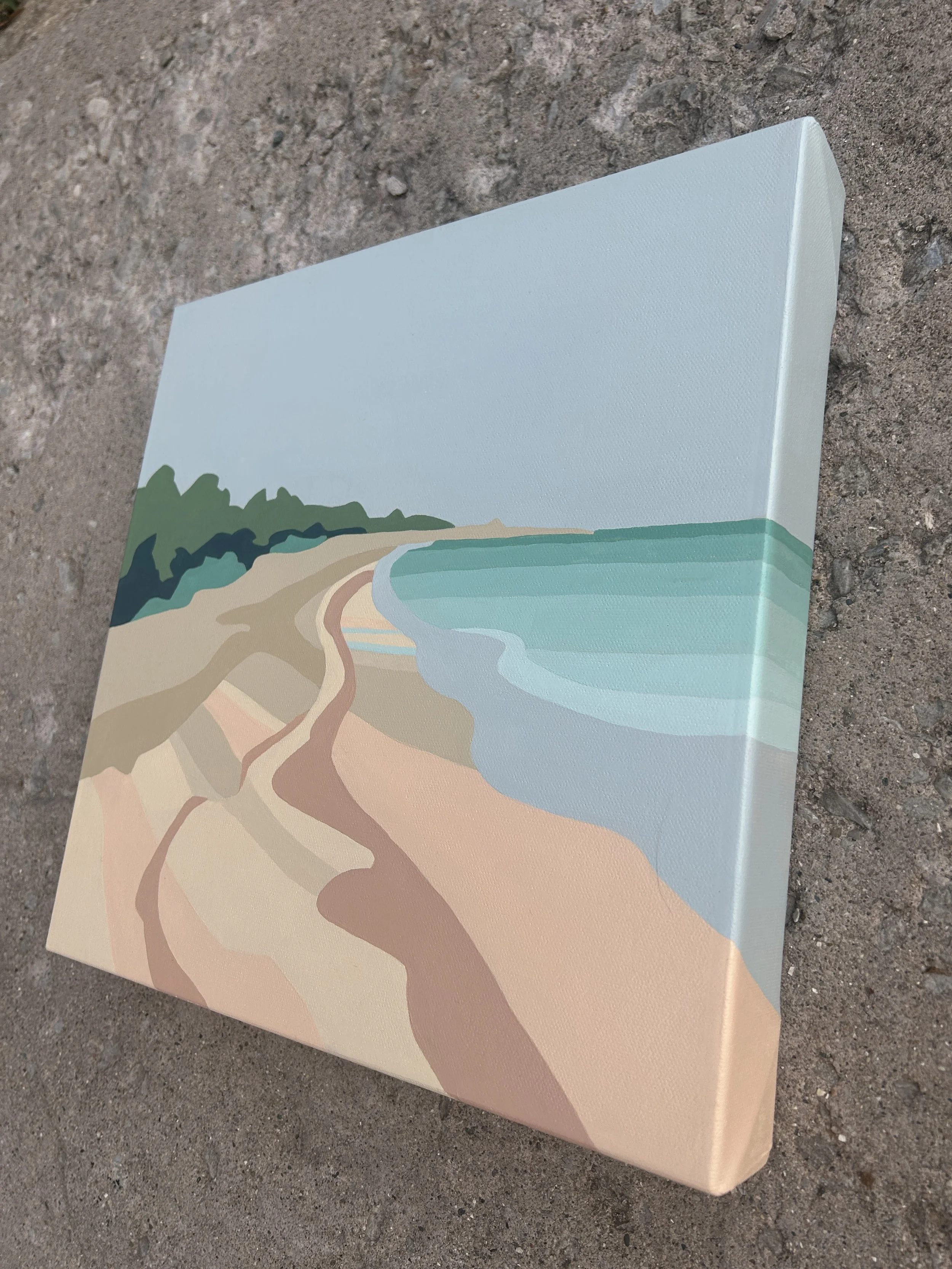 A painted canvas on the ground shows a stylized beach scene with a sandy beach, winding pathway, green bushes, and a body of water under a light blue sky.