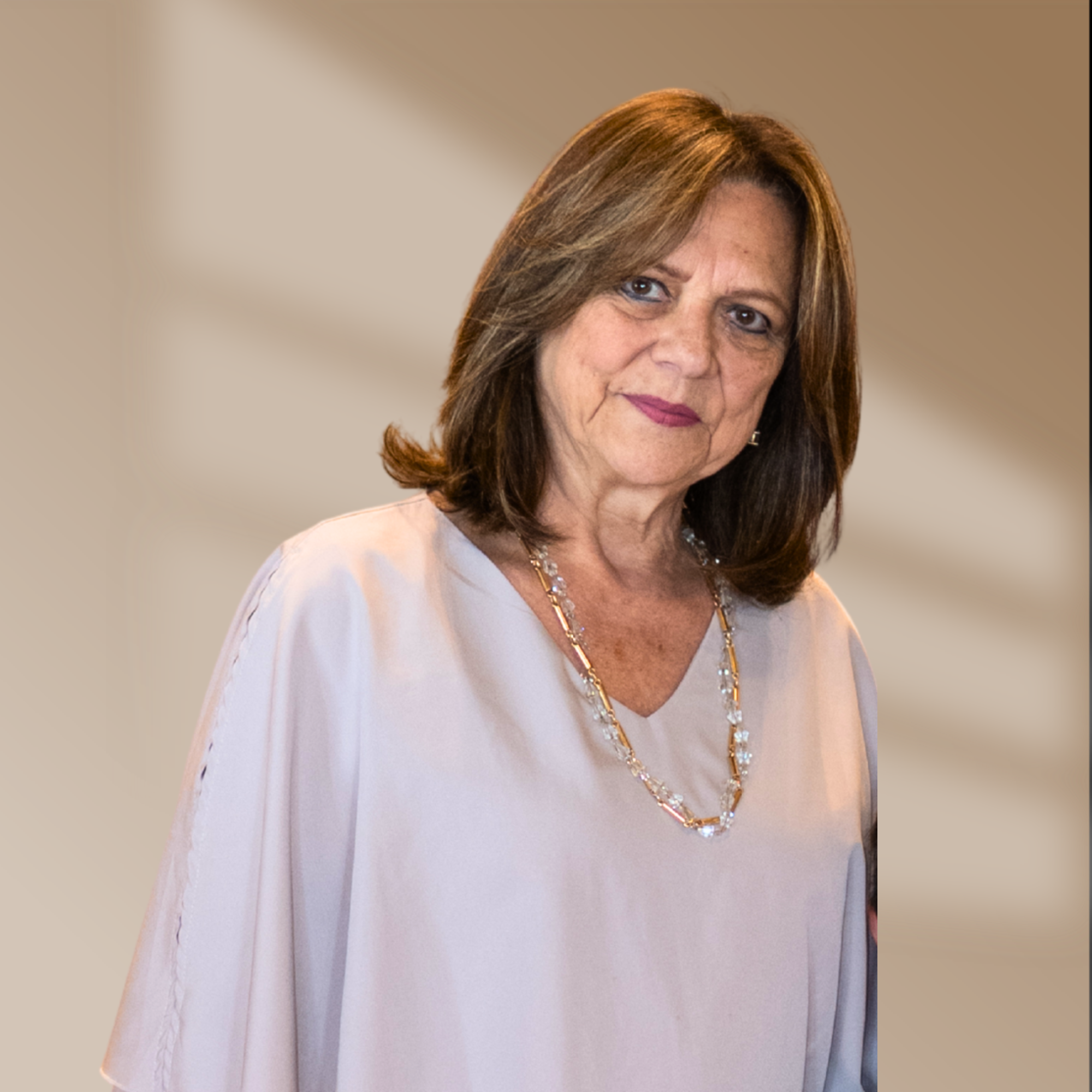 Close-up of a middle-aged woman with shoulder-length brown hair, wearing a white blouse and gold jewelry, smiling softly against a neutral background.