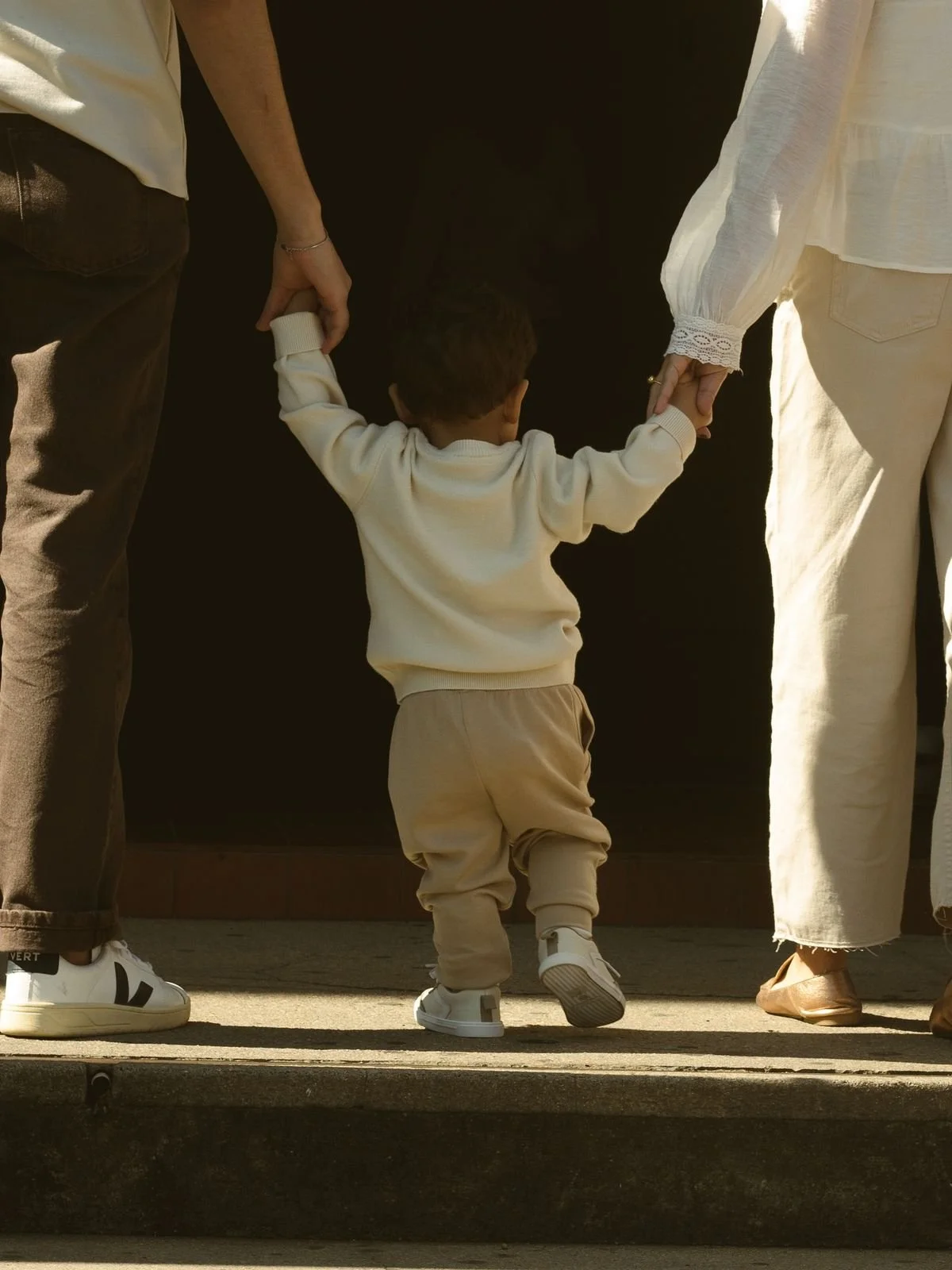 A small child holding hands with two adults, one on each side, walking together outdoors.