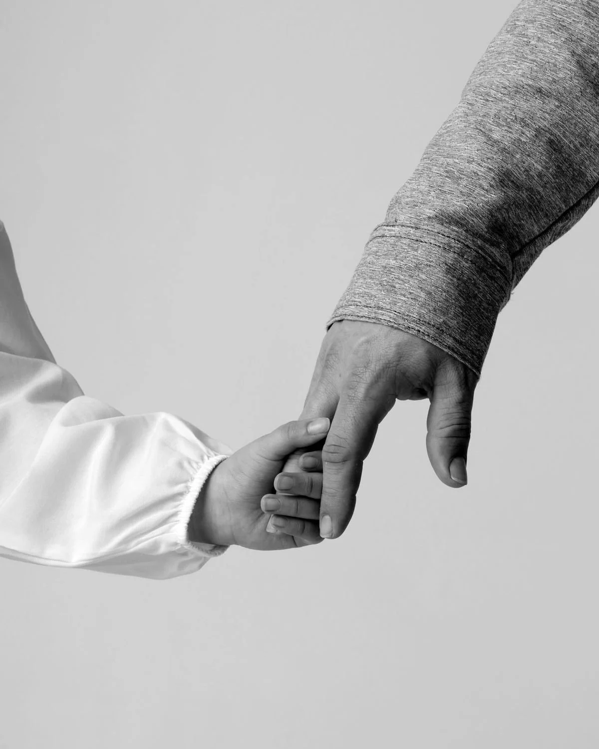 An adult and a child are holding hands, with the adult's hand gently grasping the child's hand.