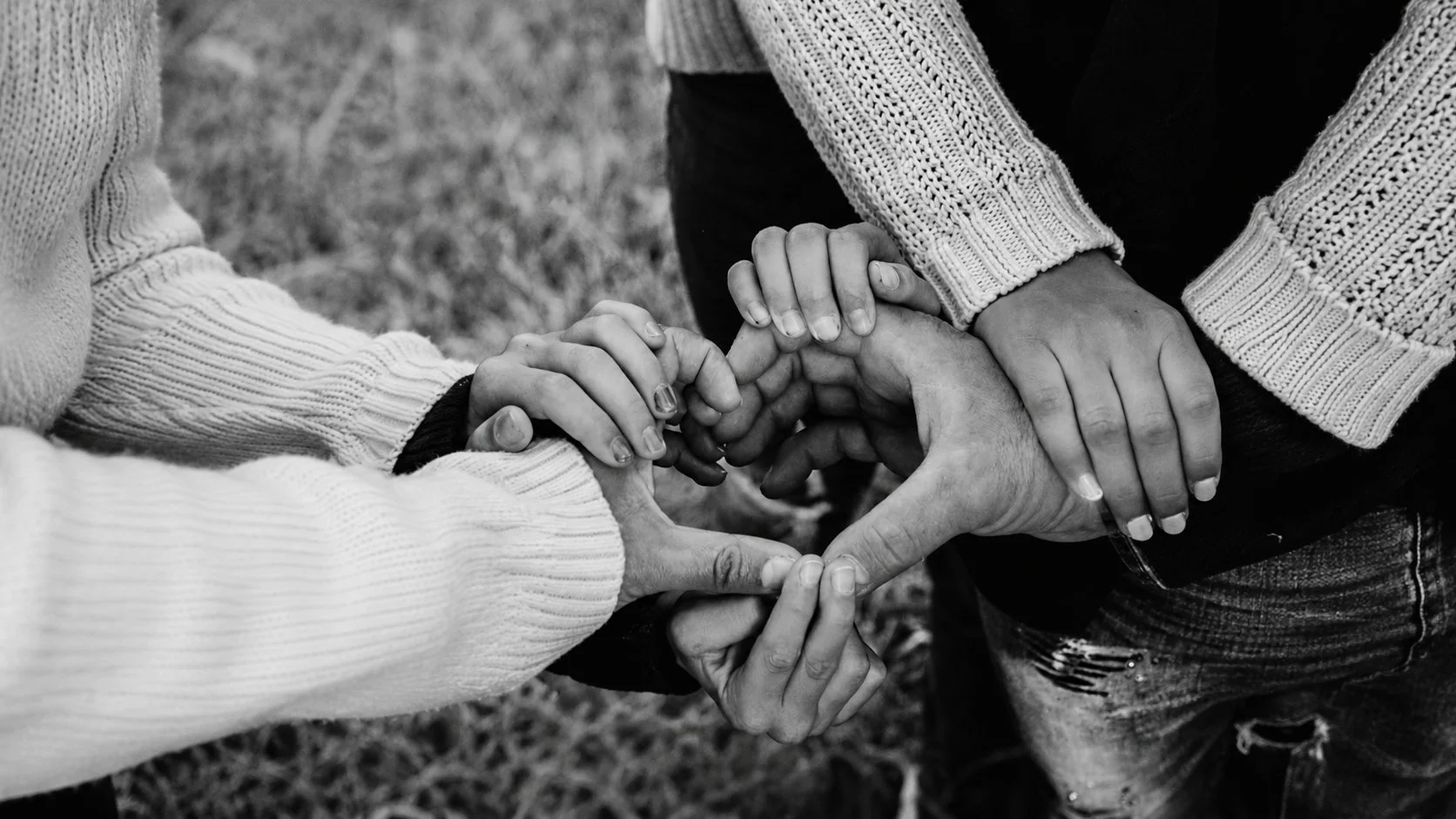 Four hands from different people forming a heart shape, captured in black and white.