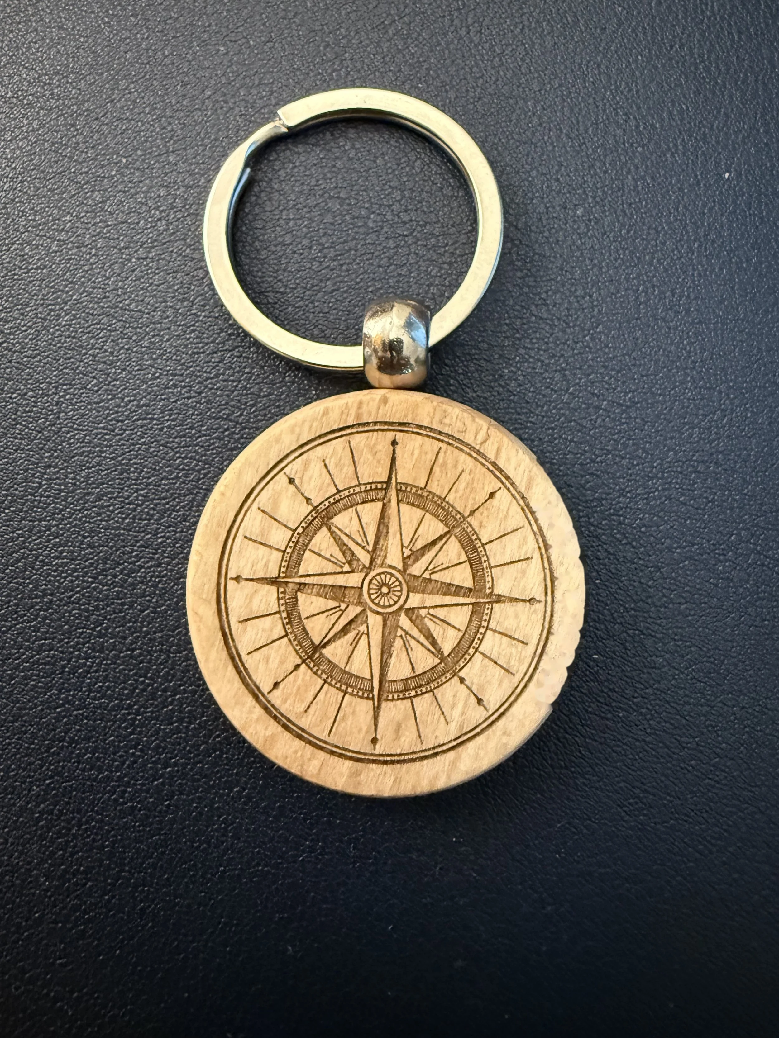 A small metal keyring attached to a round wooden keychain engraved with a compass rose design.