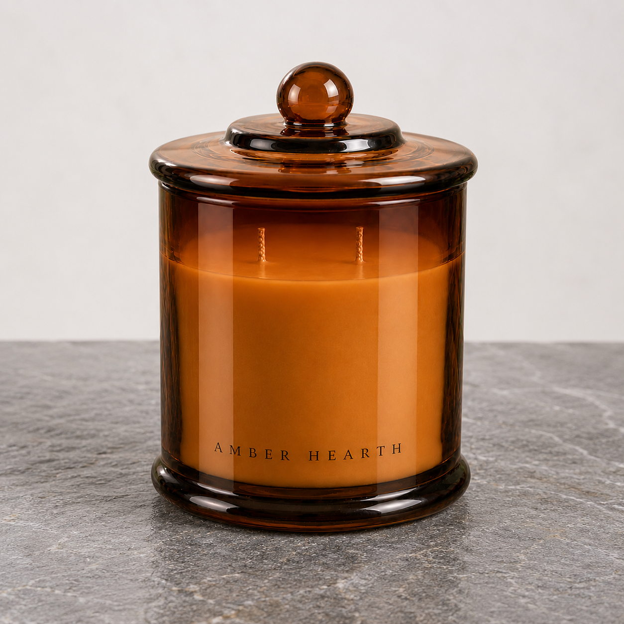 Amber glass jar candle labeled 'Amber Hearth' with a matching amber lid, placed on a gray textured surface against a plain white background.