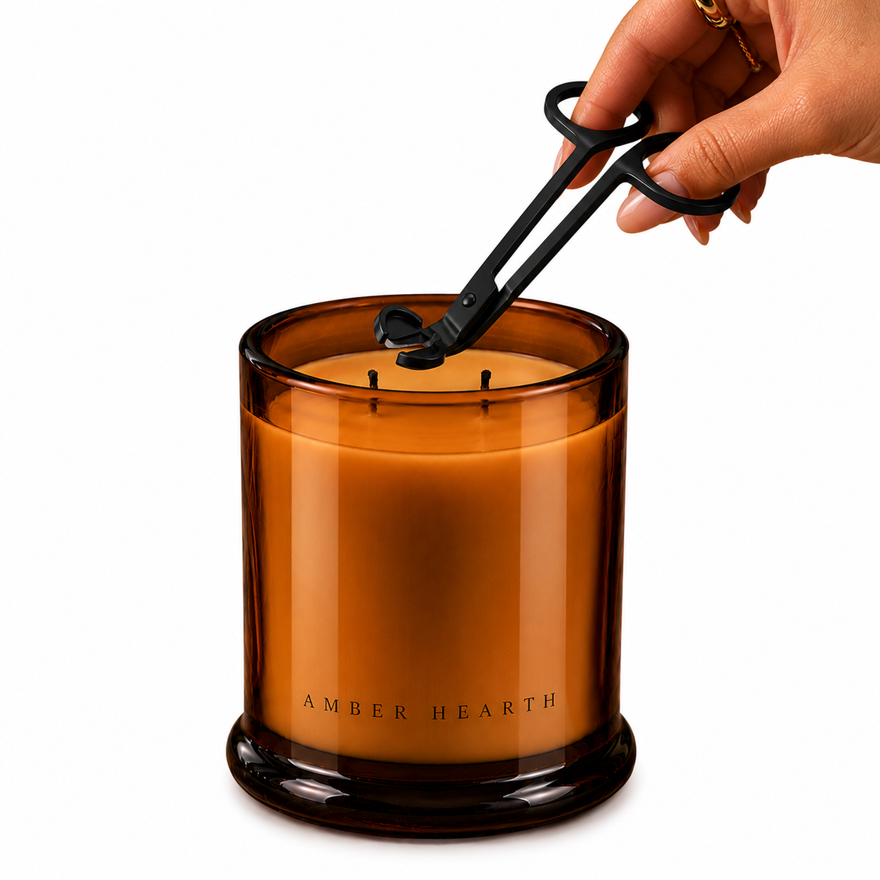 A hand trimming the wick of a large amber-colored candle labeled 'Amber Hearth' in a glass container.