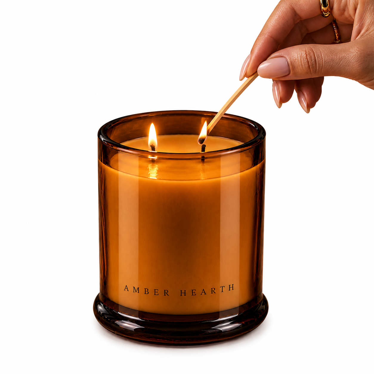 A hand lighting a candle in an amber glass candle holder with two lit wicks, labeled 'Amber Hearth'.