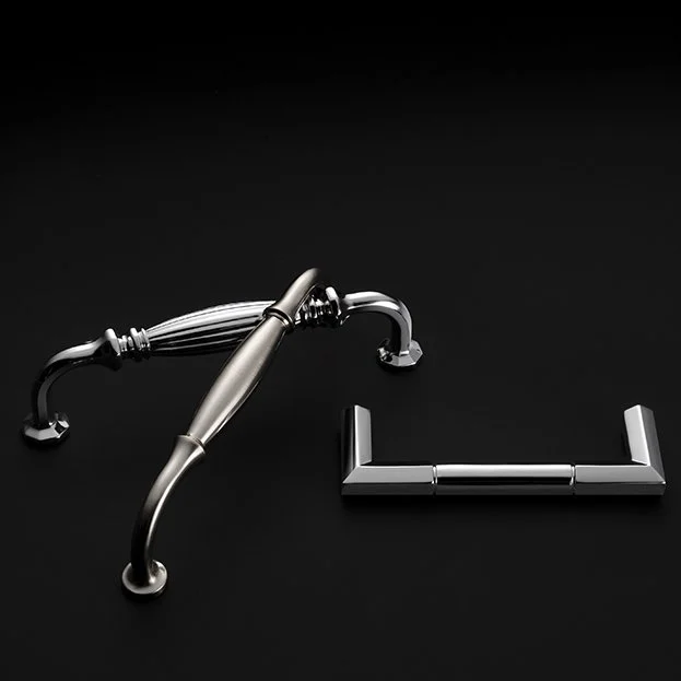 Two metallic drawer handles, one ornate and curved, the other modern and angular, are placed on a black background.