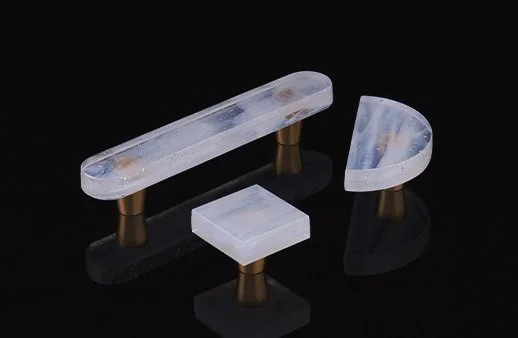Four small objects with a clear, transparent, plastic-like material on top and a metallic base, placed on a black reflective surface against a black background.