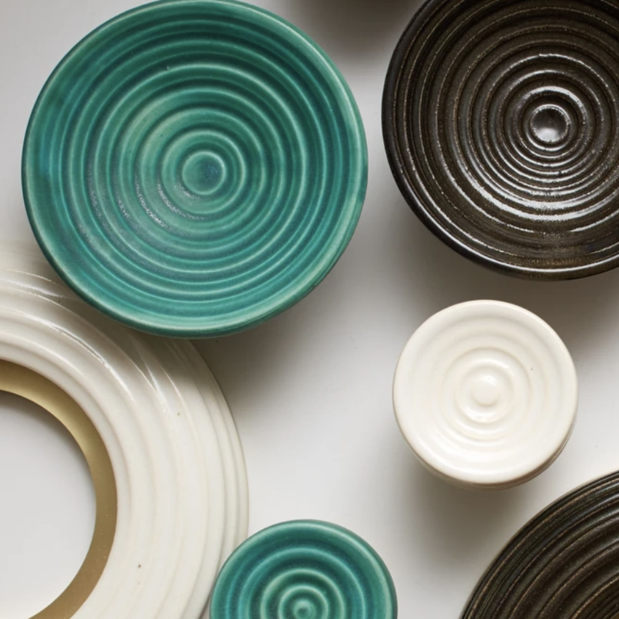 Various ceramic bowls with concentric circle patterns in colors teal, dark brown, and white on a white surface.