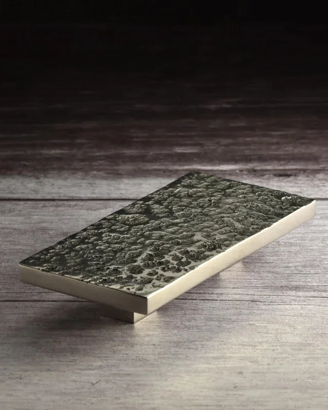 A rectangular bar of soap with a textured, dark, andlight pattern on the top surface, placed on a wooden surface.