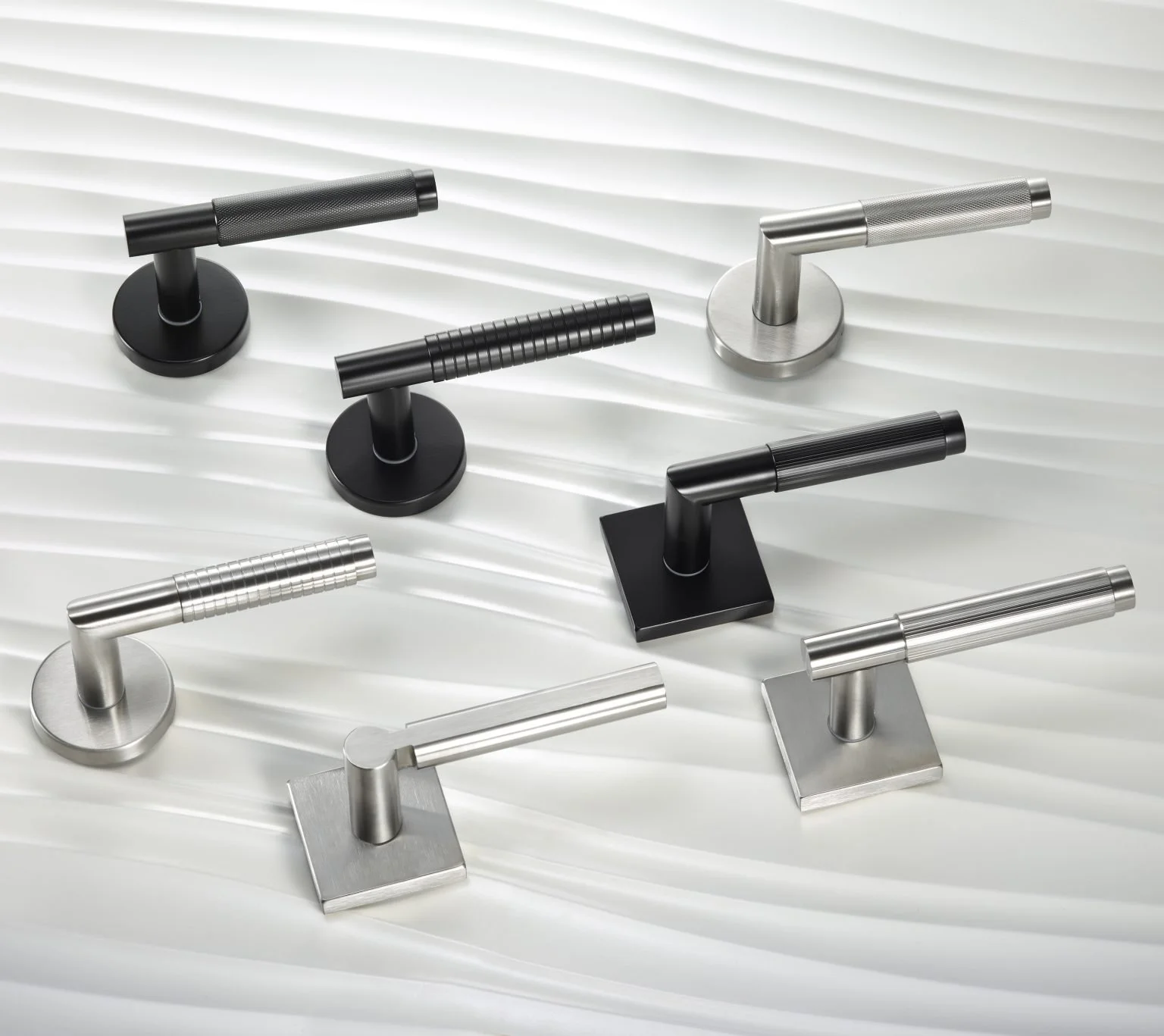 Collection of various modern door handles in black and metallic finishes on a white textured surface.