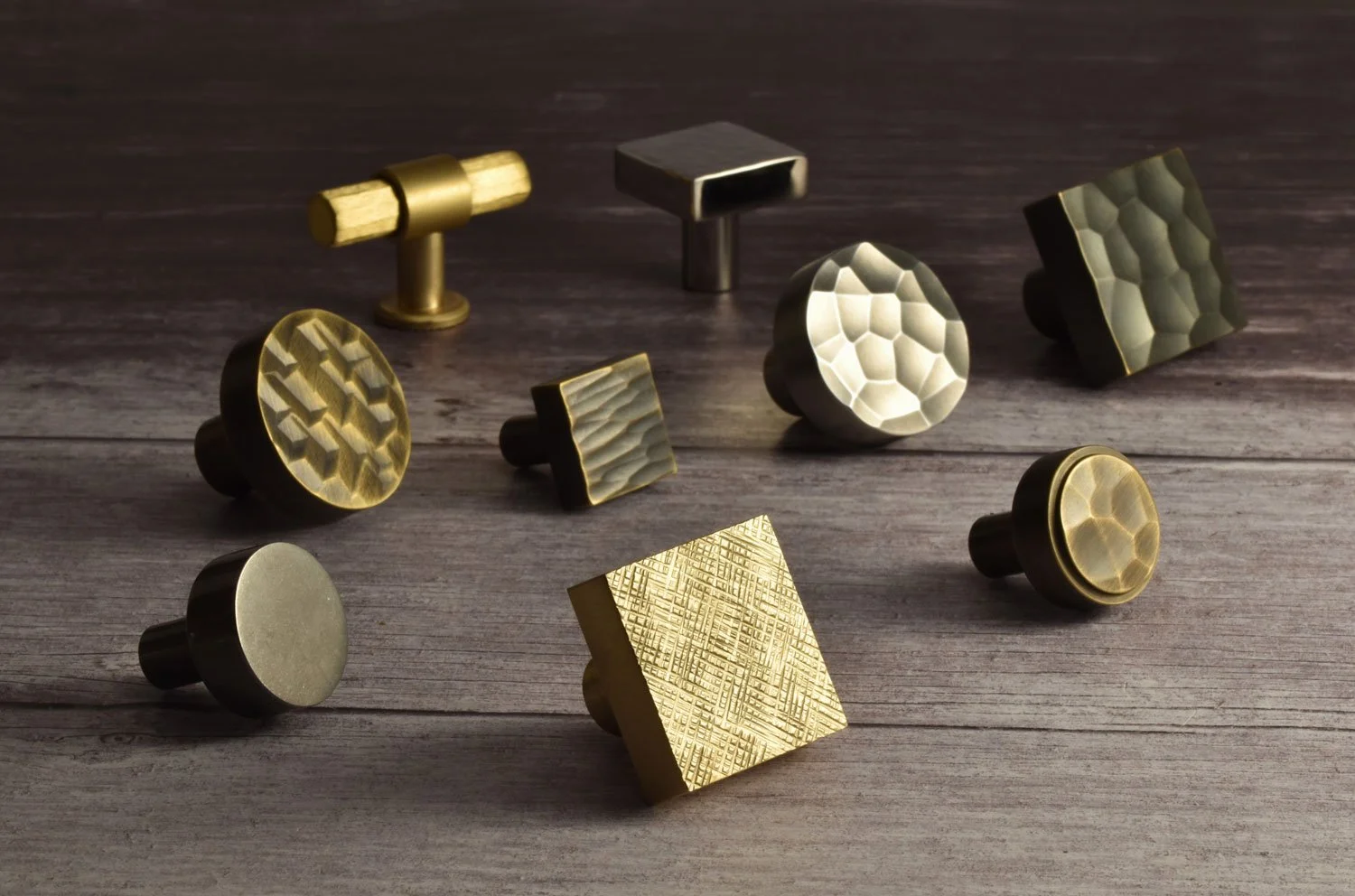 Collection of metallic drawer knobs with various textured patterns on a wooden surface.
