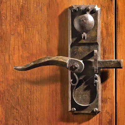 Old metal door latch and handle on a wooden door.