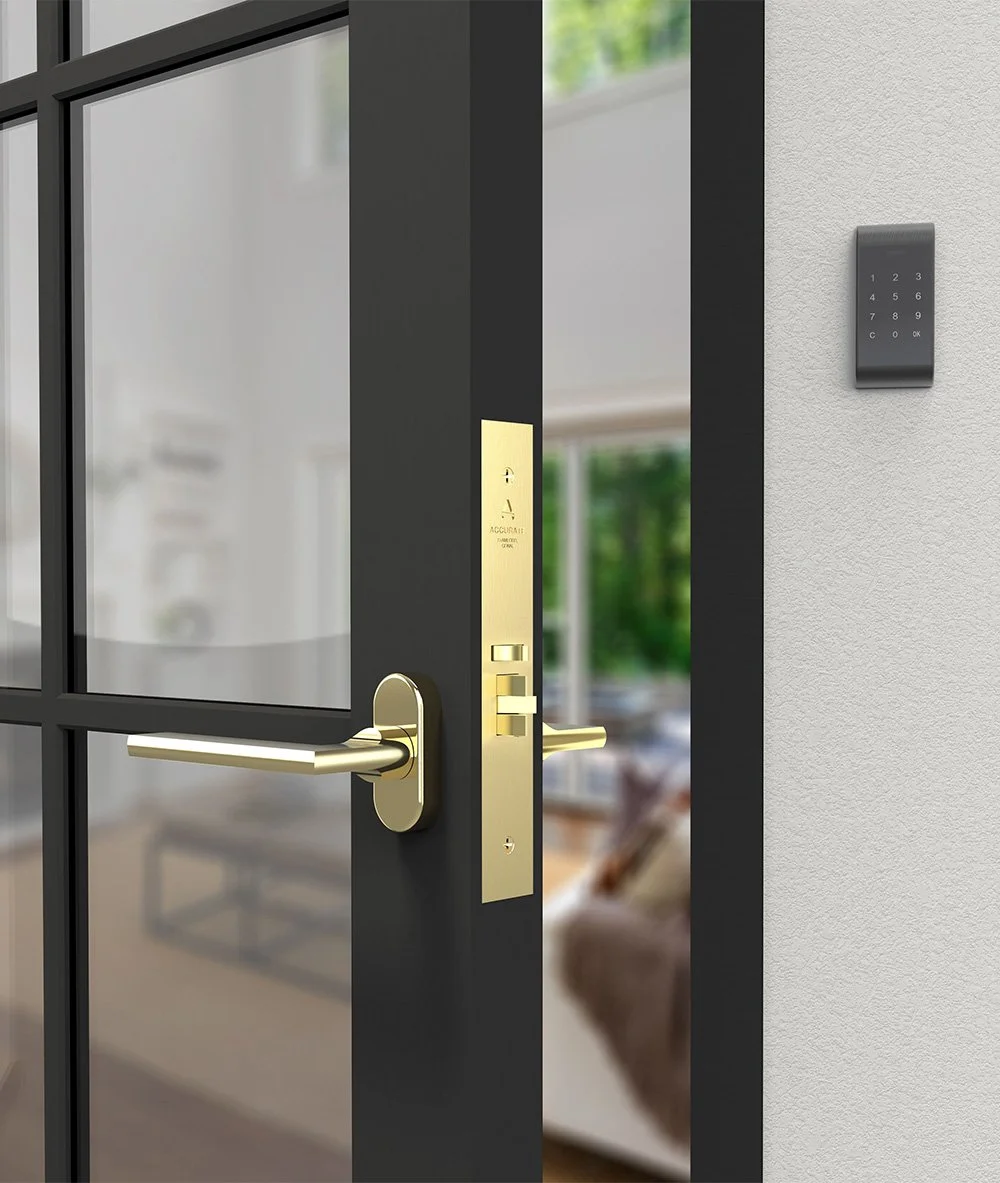 Image of a glass door with black frame and gold handles, with a keypad access panel on the wall beside it.