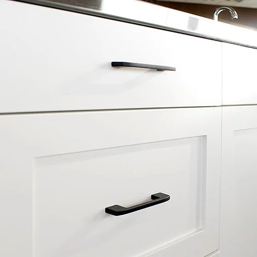 Close-up of white kitchen cabinets with black handles and a stainless steel sink in the background.