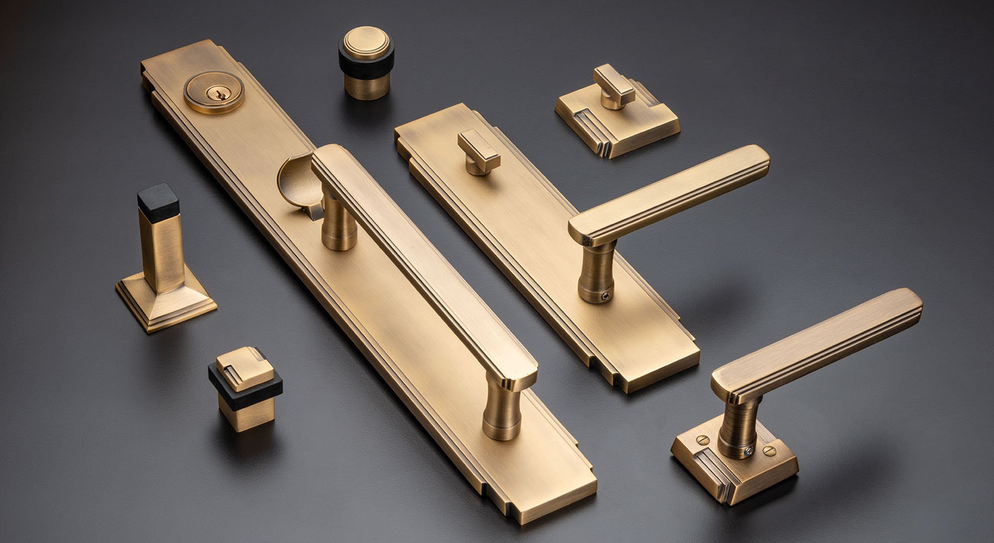 Collection of gold-finished door hardware, including handles, locks, and knobs, arranged on a dark surface.