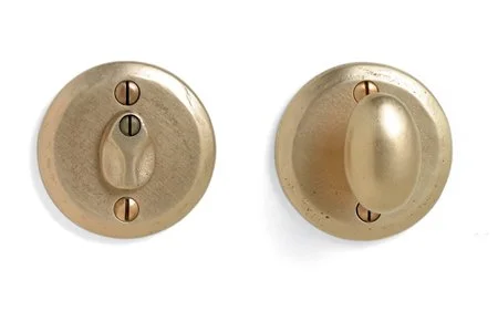 Close-up of a vintage brass door latch with a thumb turn on one side and a latch bolt on the other.
