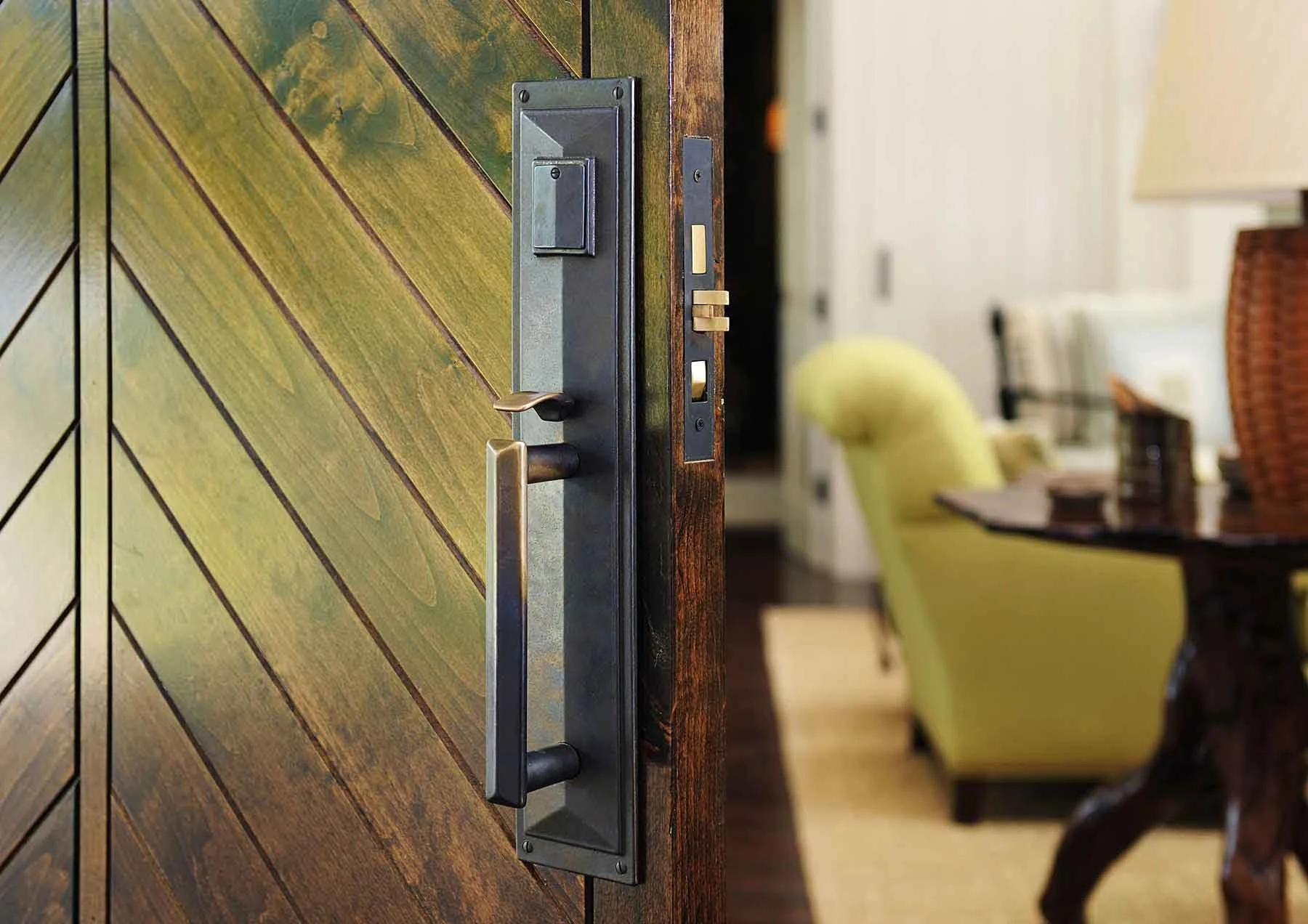 A close-up of a wooden door with a dark stain, featuring a metal door handle and a lock. The background shows a blurred interior with chairs and a table, suggesting a dining or meeting area.