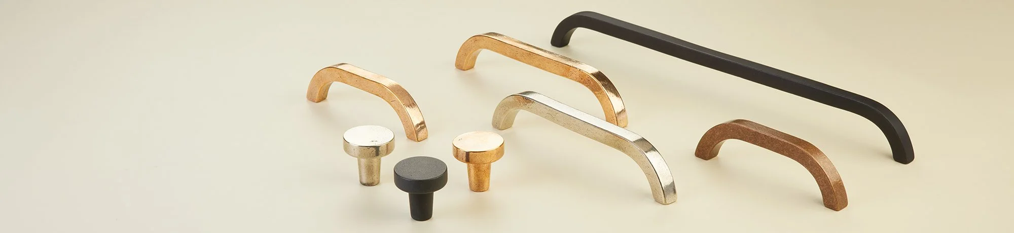 Assorted cabinet pulls in various shapes, sizes, and finishes, including black, brushed gold, chrome, and bronze, arranged on a light background.