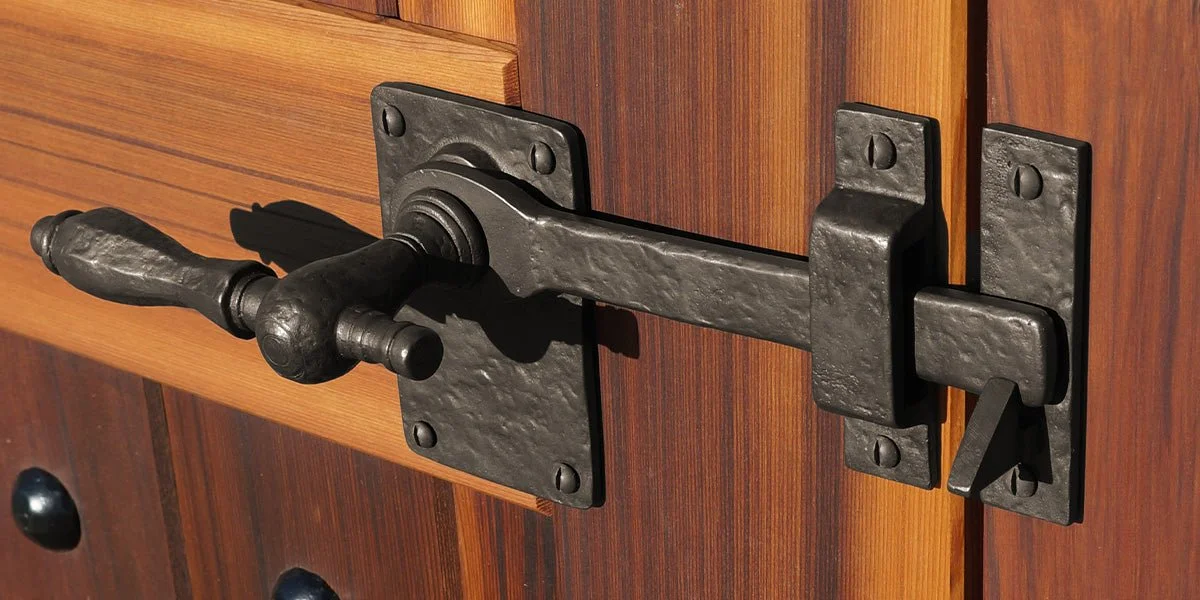 Close-up of a black, rustic, wrought iron latch lock on a wooden door.