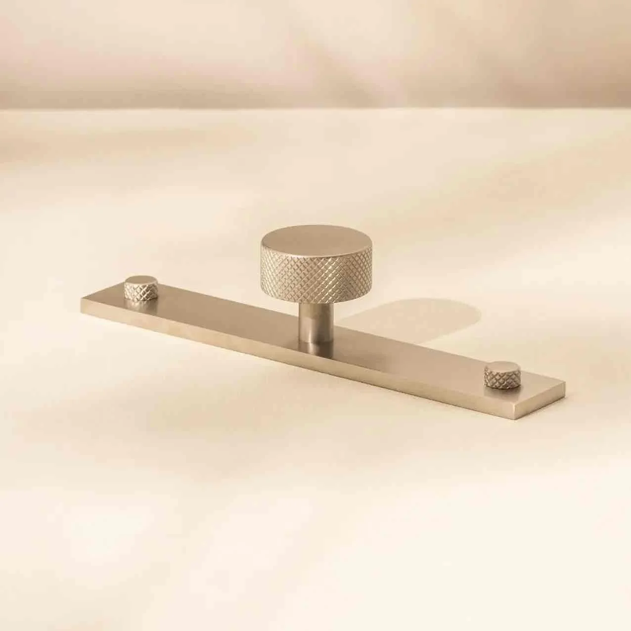 A metallic, minimalist wall-mounted fixture with a large central knob and two smaller knobs on either end.