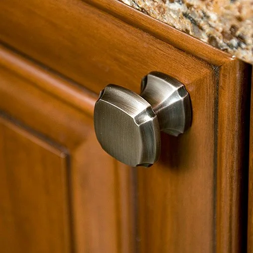 Close-up of a stainless steel cabinet knob on a wooden kitchen cabinet.