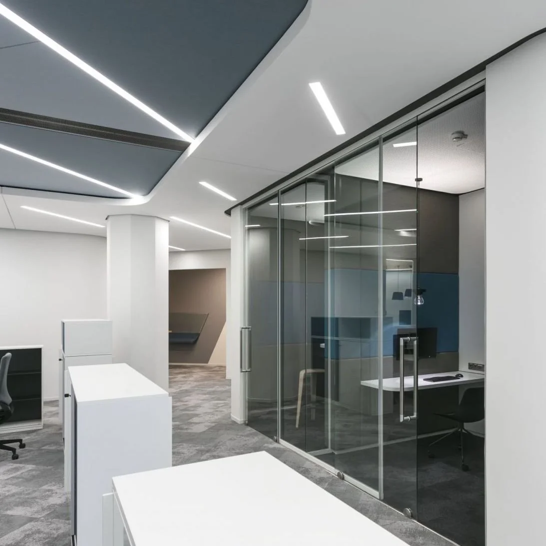 Modern office space with glass enclosed meeting room and white desks.
