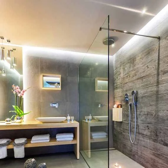 Modern bathroom with a wooden vanity, white towels, pink orchids, and a glass-enclosed shower with wall-mounted shower fixtures.