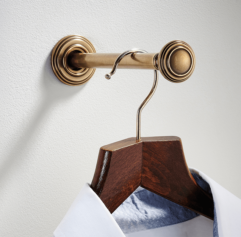 A gold-colored wall-mounted closet rod with a wooden hanger holding a dress shirt.
