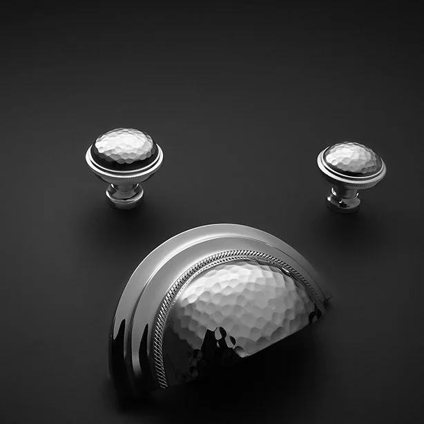 Three silver golf trophies placed on a black surface, with two smaller ones in the background and a larger one in the foreground, all with hammered metal textures.