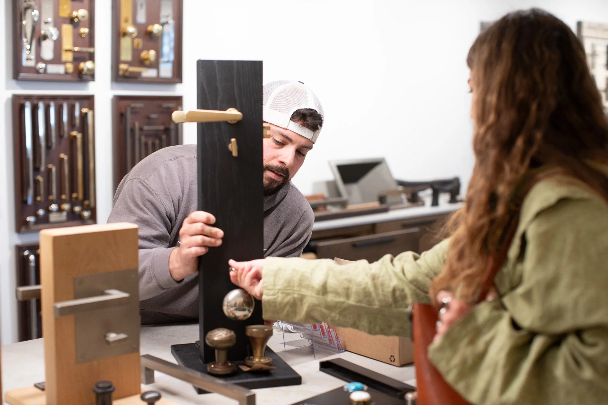 A man and a woman are playing chess at a store counter, with a chess clock and wooden chess pieces between them, and shelves with hardware tools in the background.