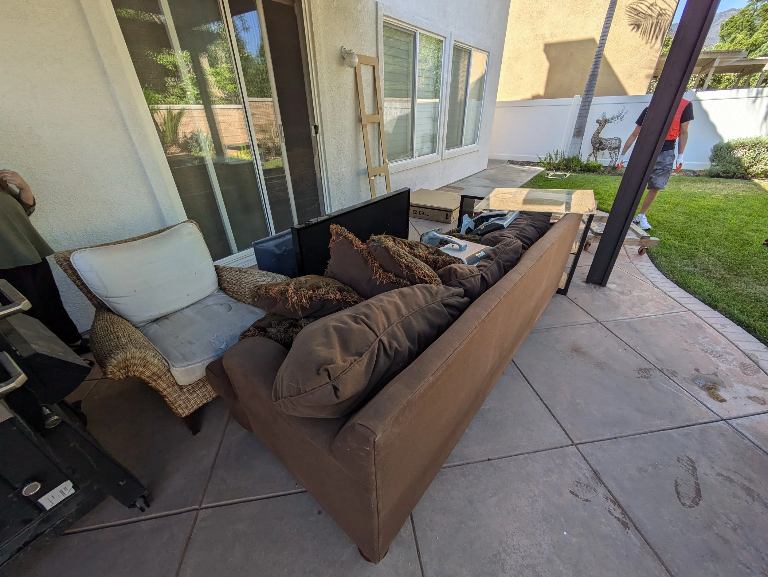 Backyard patio with outdoor furniture, a tarp-covered table, a box, and a person standing near a decorative deer mural on a white fence.