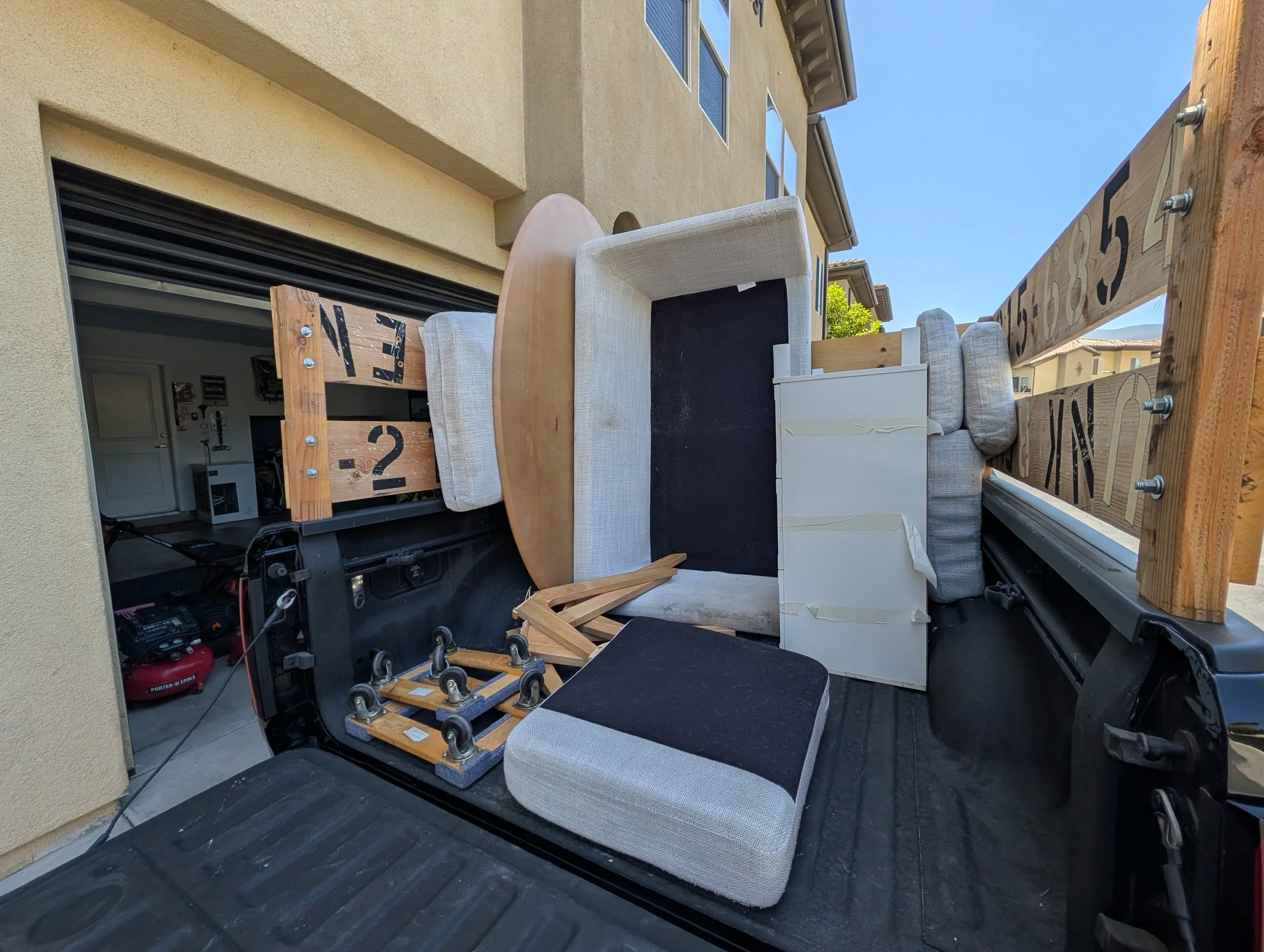 View of a balcony with furniture and construction materials, including a sofa, a small table, and wooden boards, each labeled with numbers, under clear blue sky.