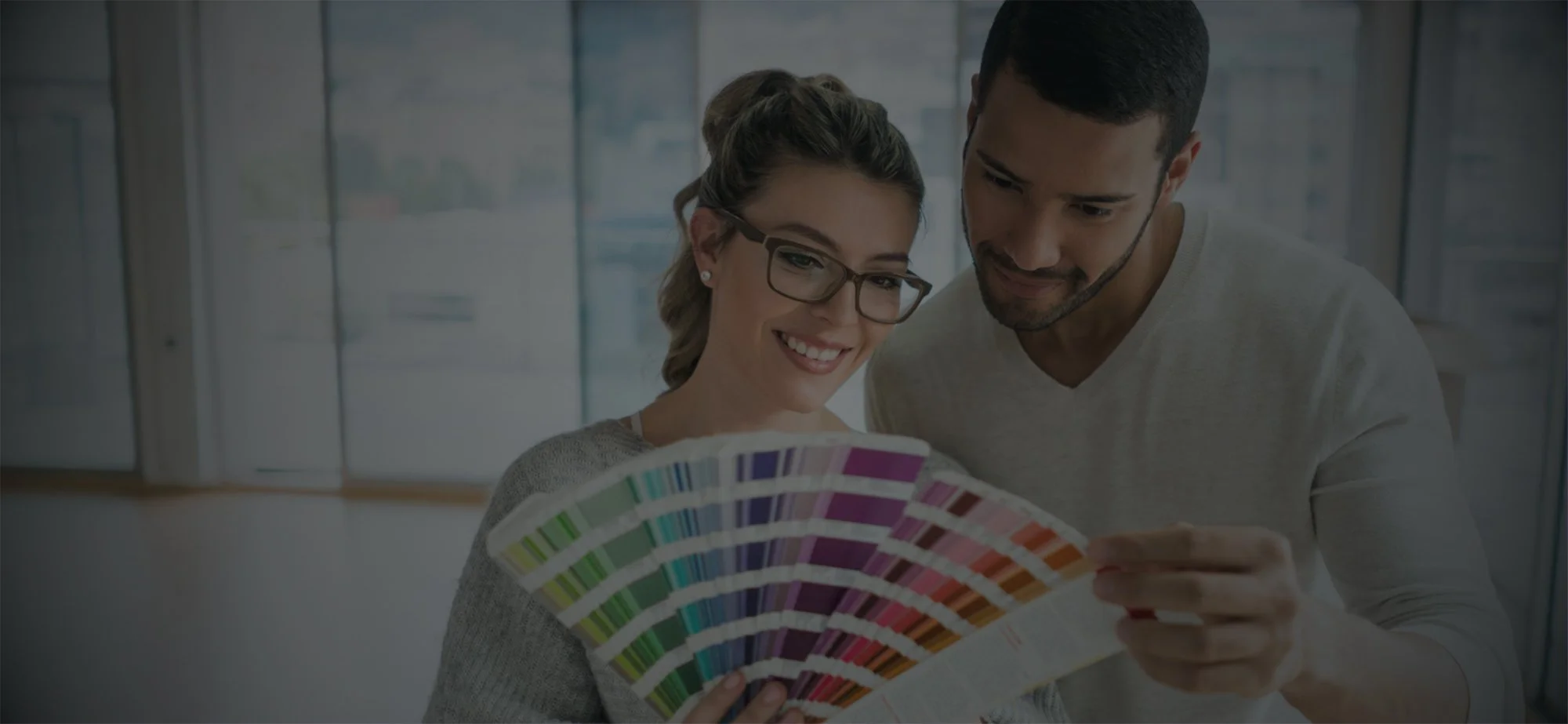 A smiling woman with glasses and a man look at a colorful paint swatch fan picking out home paint color with local painter in Redding
