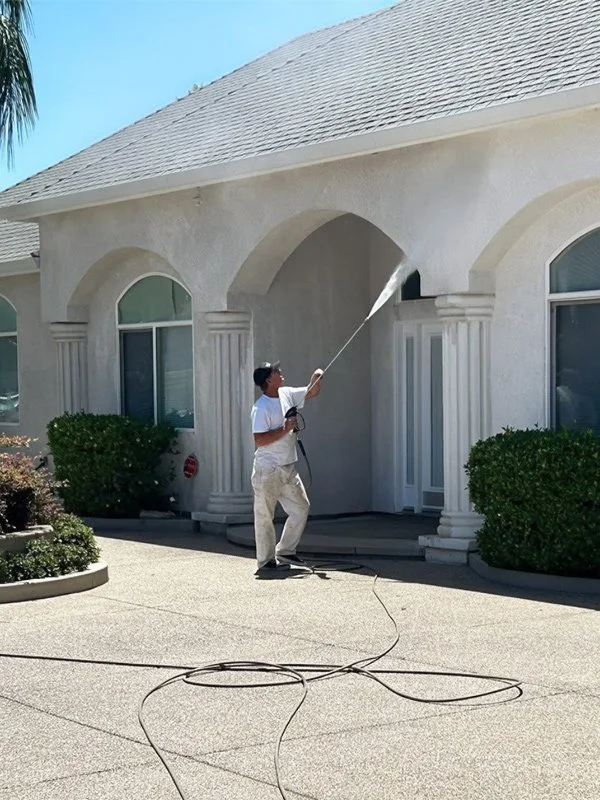 Steven Francis Painting power washes the exterior wall of a white house before painting residential home