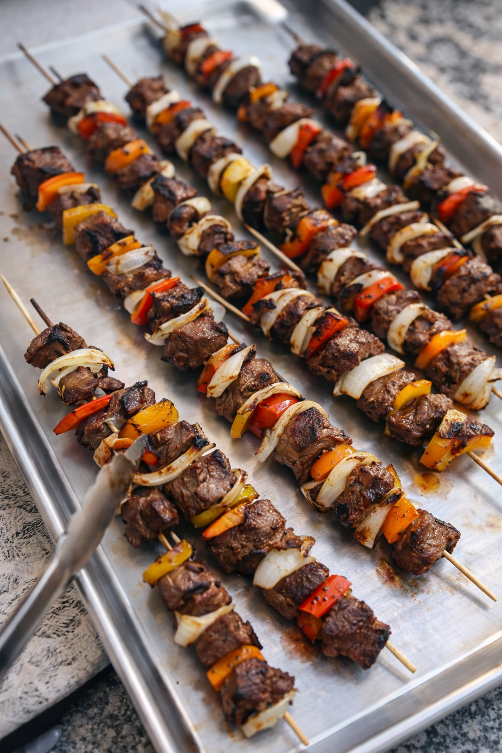 Close-up of grilled lamb kebabs with bell peppers and onions on skewers, arranged on a baking sheet.