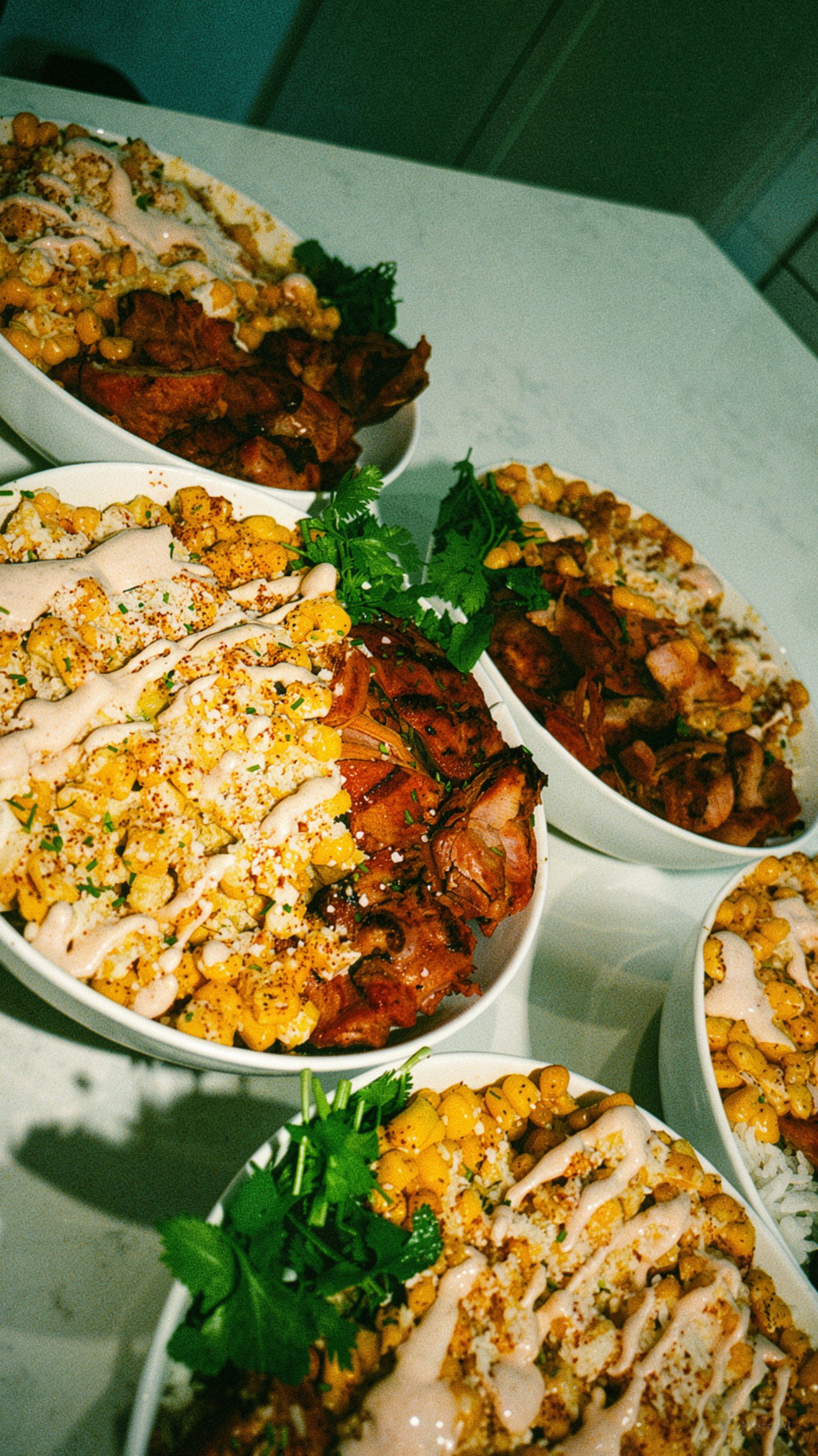 Bowls with chicken, rice,  elote corn, and toppings with cilantro garnish.