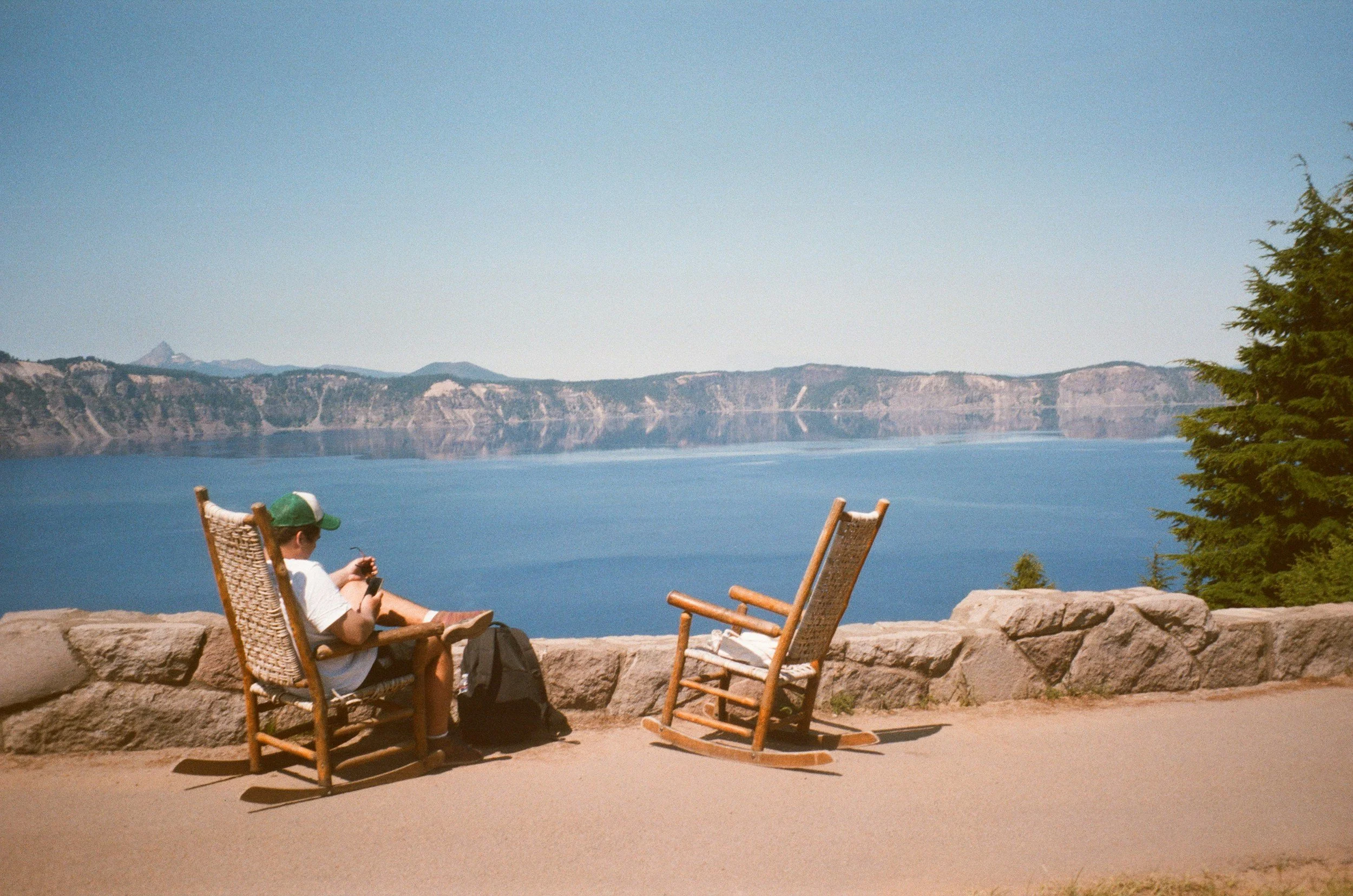 film photo of man in chair by lake and mountains