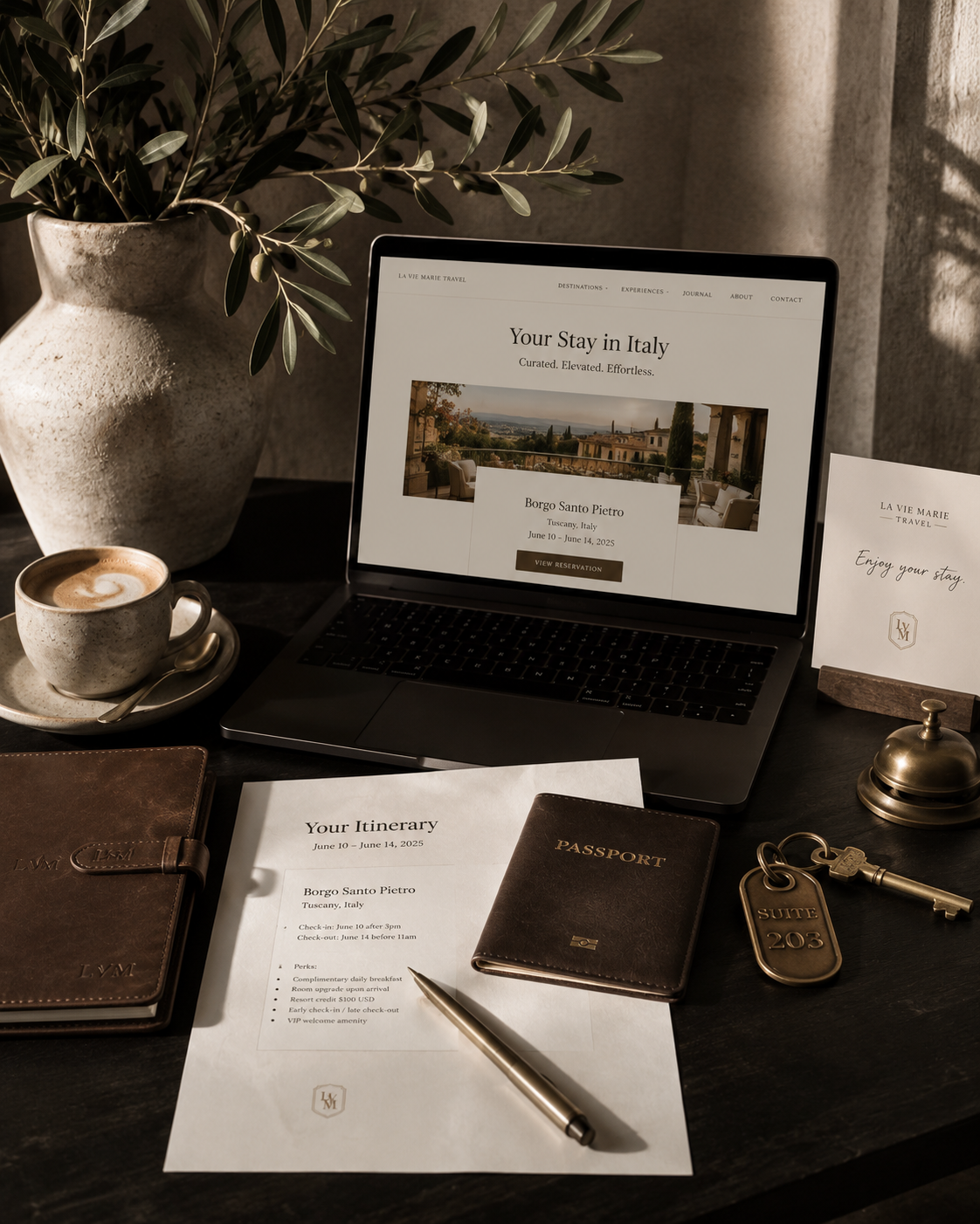 A workspace with a laptop displaying an Italy travel website, a cup of coffee with latte art, a potted plant, travel documents including a passport, itinerary, and reservation details, a pen, a bell, a key, and a greeting card that says "Enjoy your stay" on a dark wooden desk.