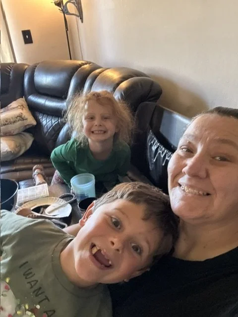 A woman and two children taking a selfie in a living room. The woman is smiling, and the children are making playful faces.
