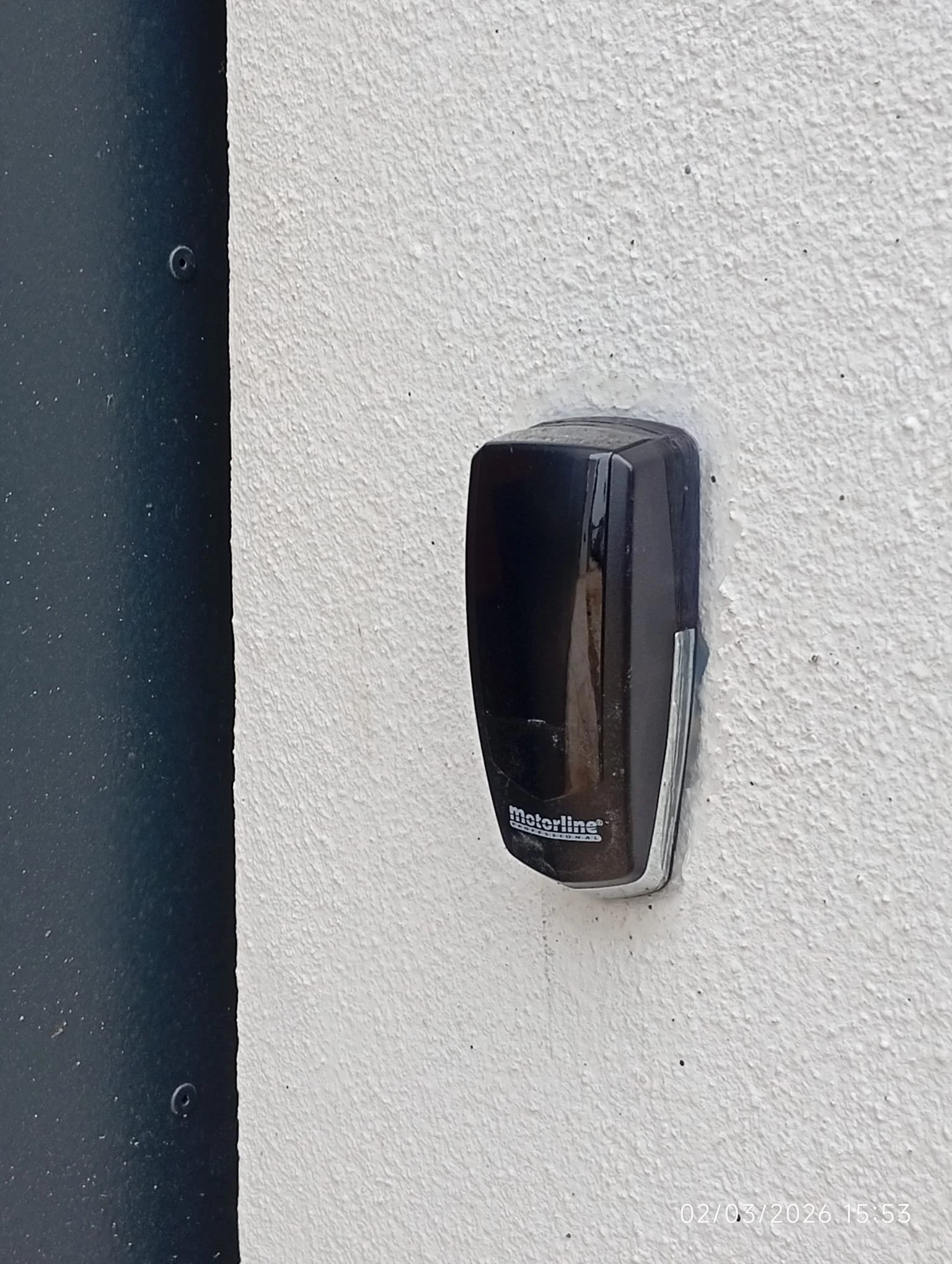 Fechadura eletrônica preta na parede branca, com logo Motorline, perfil digital ou código na parte inferior. Data e hora no canto inferior direito.