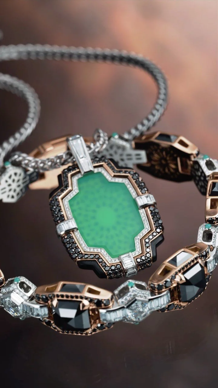 Jewelry necklace with large green gemstone pendant surrounded by black and clear stones, along with other decorative elements.