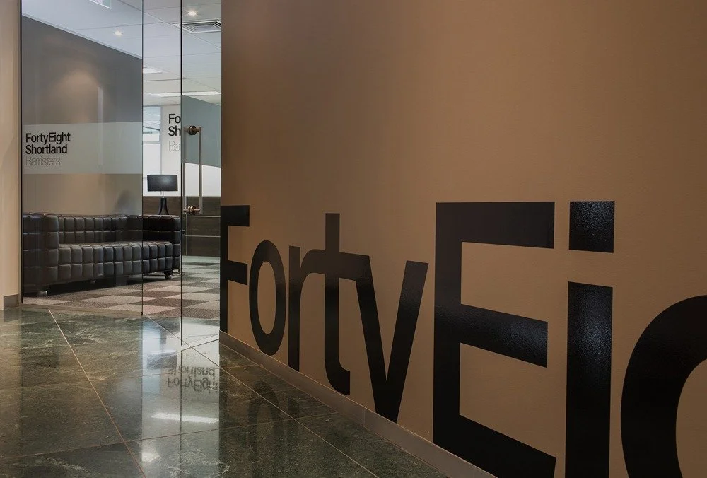 Office interior with glass door and wall featuring large black letters spelling 'Forty Five' and a seating area with black leather couch and a small table with a computer monitor.