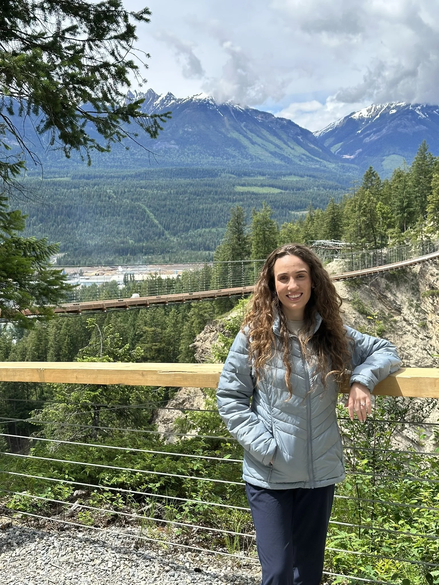 woman standing in front of a suspension bridge and mountains in Canada
