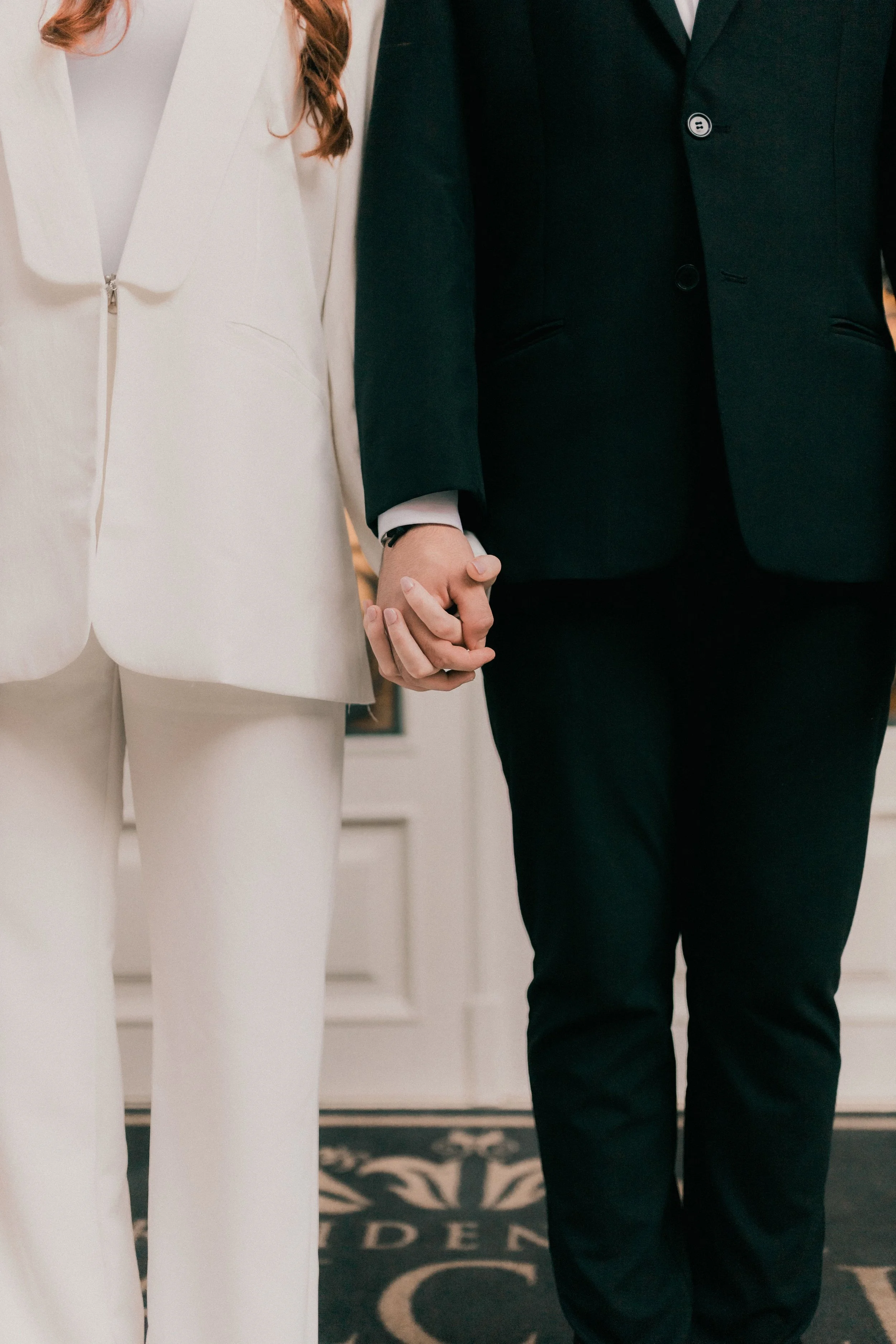 husband and wife on wedding day holding hands in front of white door, only lower bodies visible