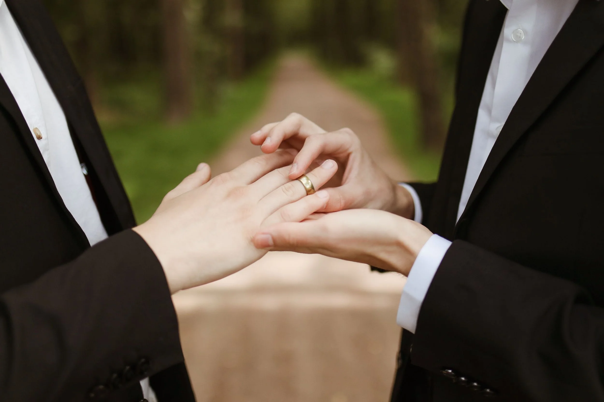 close up of a husband sliding a gold ring on his husband's finger