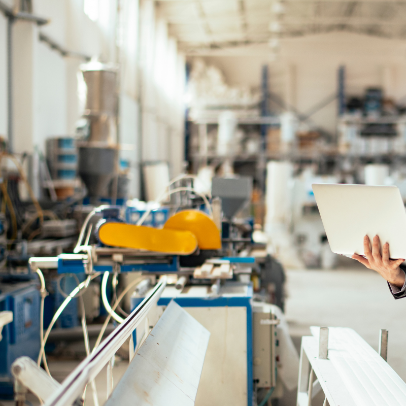 A person holding a laptop in a manufacturing or industrial workshop with machinery and equipment.