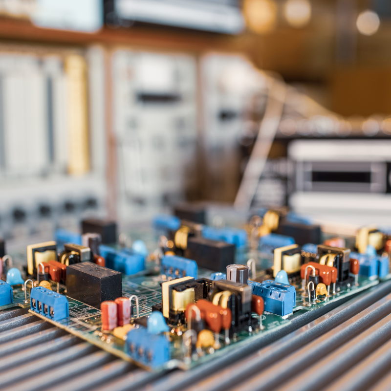 Close-up of an electronic circuit board with colorful components, placed on a metallic surface in what appears to be an electronics workshop.