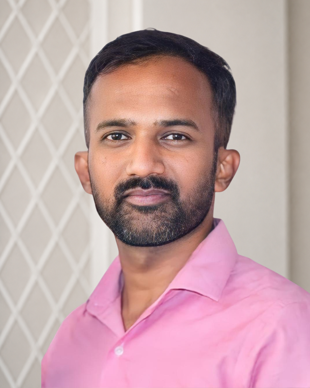 Headshot of a man with short black hair, a beard, and mustache, wearing a pink collared shirt, standing in front of a lattice background.